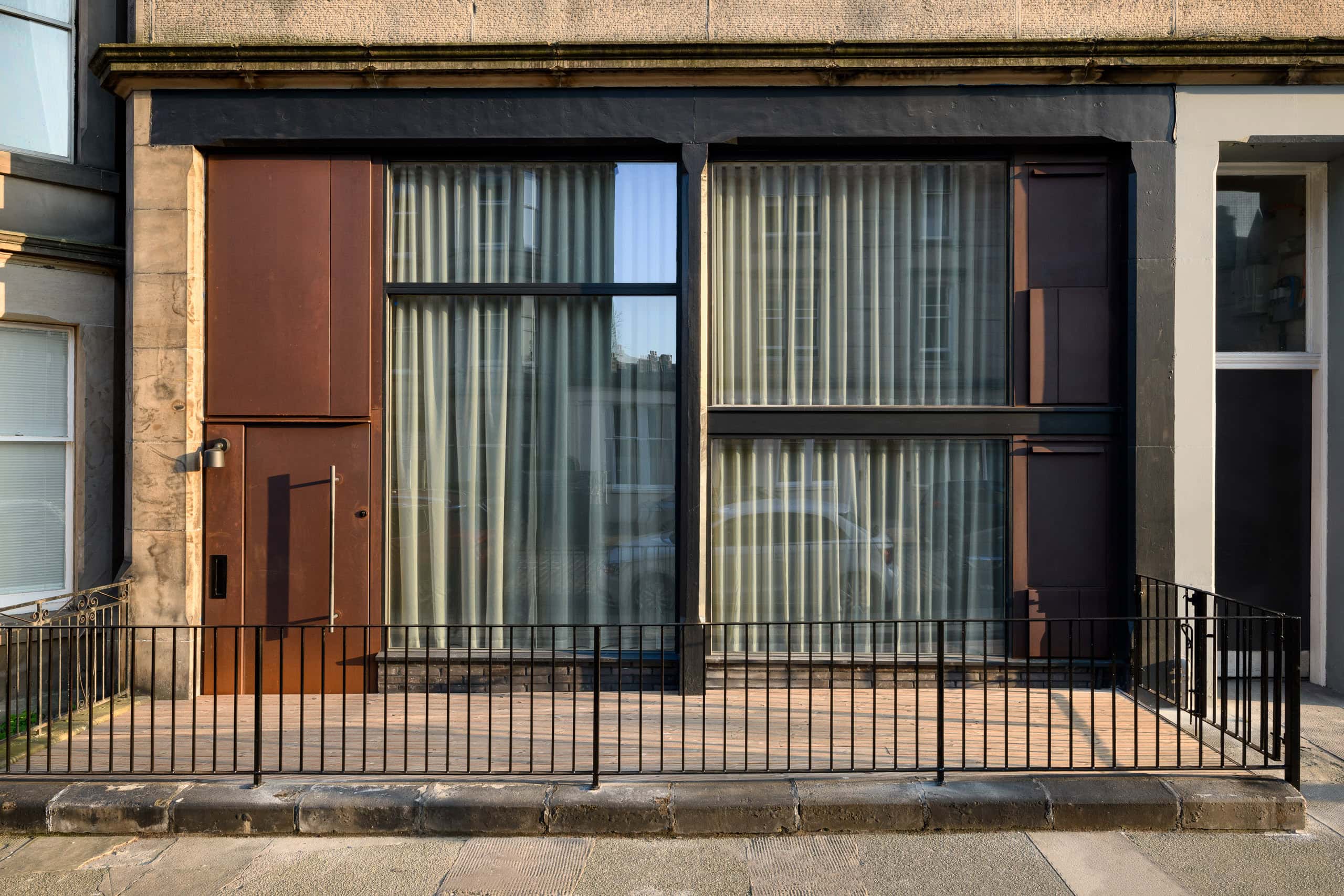Modern storefront with large glass windows and brown shutters in an urban setting.