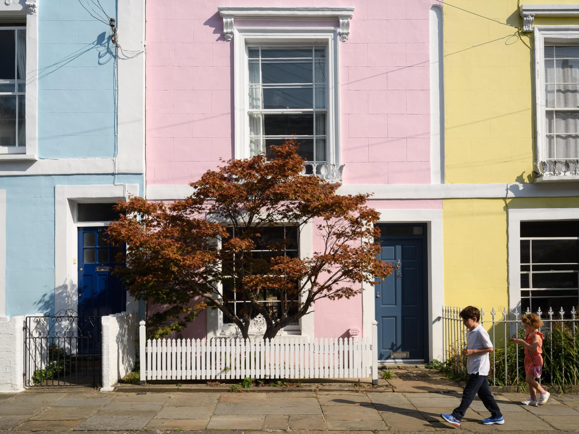 Bright pastel-coloured terraced houses with children playing outside on a sunny day.
