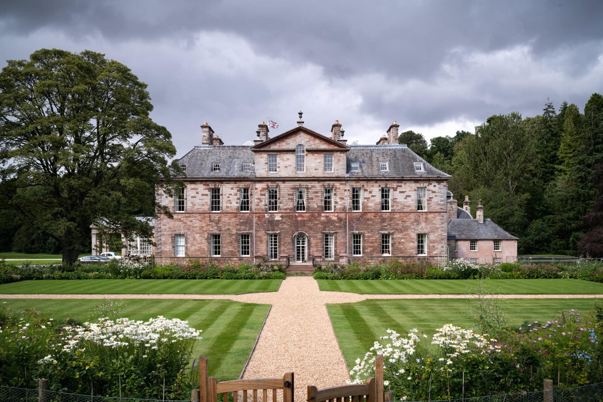 Historic mansion with landscaped gardens and cloudy sky in the background.
